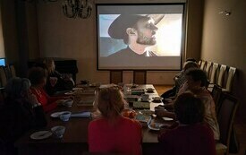 Kobiety siedzą przy stole i oglądają film na dużym ekranie