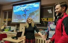 Bibliotekarka wita gościa na spotkaniu. W tle książki oraz prezentacja na rzutniku. 