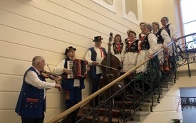 Zesp&oacute;ł folklorystyczny w strojach ludowych stoi na schodach