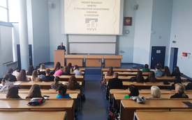 Aula studencka wypełniona uczestnikami spotkania. Starszy Pan w garniturze na m&oacute;wnicy. 