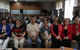 Kilkanaście ludzi siedzi na krzesłach i pozuje do wsp&oacute;lnego zdjęcia. 