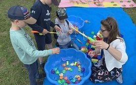 Kobieta i trzech chłopc&oacute;w z wędkami podczas zabawy w łowienie rybek.