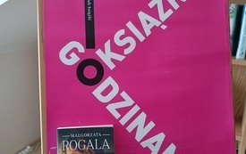 Na tablicy plakat informujący o spotkaniu, książka i logo DKK.