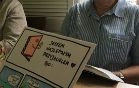 Po prawej stronie siedzi kobieta przy stole, po lewej ręka trzymająca kartkę papieru z ilustracjami dotyczącymi korzyści z czytania książek.  