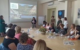 Sala konferencyjna. Prezentacja multimedialna. Uczestniczki warsztat&oacute;w słuchają przemowy Pani Dyrektor Bibilioteki.