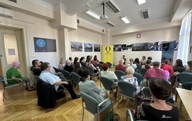 Sala konferencyjna. Mężczyzna i kobieta siedzący na fotelach. Liczna widownia. 