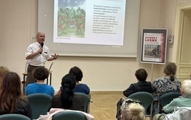 Sala konferencyjna. Prezentacja multimedialna. Mężczyzna przemawia do mikrofonu. W tle widownia.