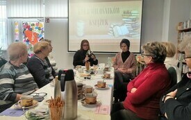 Bibliotekarka z książką w ręku. Czytelniczki przy stoliku.