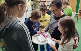 Bibliotekarka rozdaje dzieciom materiały promocyjne z Dyskusyjnych Klub&oacute;w Książki. 