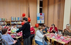 Kobieta rozdaje kolorowe pudełka wśr&oacute;d uczestnik&oacute;w spotkania