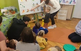 Bibliotekarka wskazuje na tablicy zdjęcia dinozaur&oacute;w. 