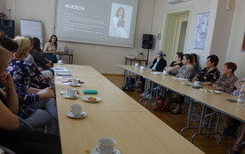 Grupa ludzi siedzi przy stole, ogląda slajd na ekranie. 