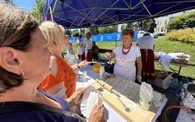 Pani z koła gospodyń wiejskich robi proziaki na stolnicy. Rozmawia z kobietami. 