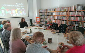 Sala biblioteczna, przy stoliku seniorki z bibliotekarką. 