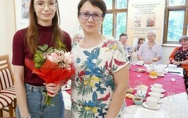 Maria Karnas i bibliotekarką stoją obok siebie, młoda dziewczyna trzyma bukiet kwiat&oacute;w. 