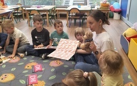 Bibliotekarka czyta dzieciom książkę, dzieci siedzą w okręgu. 