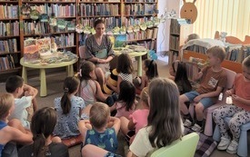 Bibliotekarka prowadzi zajęcia czytelnicze. Dzieci słuchają. 