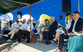 Grono os&oacute;b siedzących na krzesłach pod namiotem i czytających. 