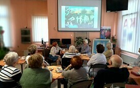 We wnętrzu biblioteki uczestnicy wykładu patrzą na prezentację. 