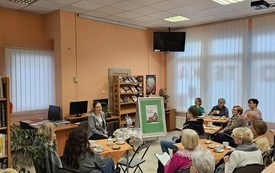 Grupa os&oacute;b sidzi przy stolikach w bibliotece i słucha wykładu