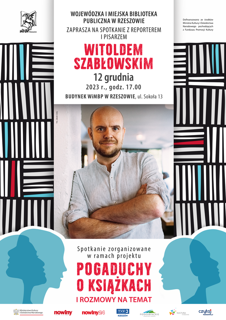 Mężczyzna z zarostem w jasnej koszuli, z założonymi rękami oparty ramieniem o ścianę.